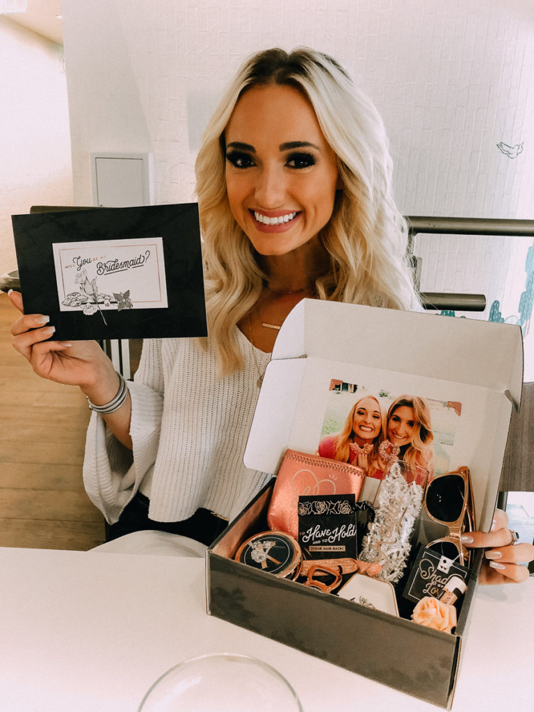 How to Ask your Bridesmaids featured by top US lifestyle blogger Audrey Madison Stowe; Blonde woman smiling with box