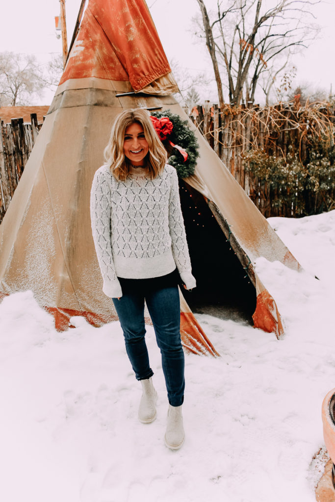 How To Cuff Women's Jeans featured by top US fashion blogger Audrey Madison Stowe; Woman standing in front of tepee wearing a sweater and jeans.