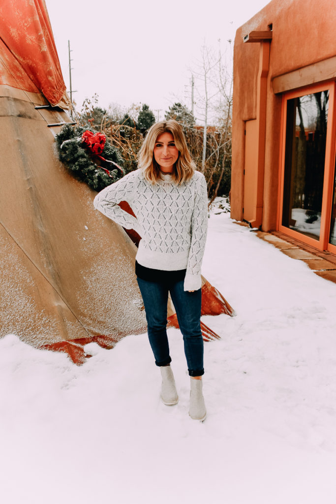 How To Cuff Women's Jeans featured by top US fashion blogger Audrey Madison Stowe; Woman standing in front of tepee wearing a sweater and jeans.